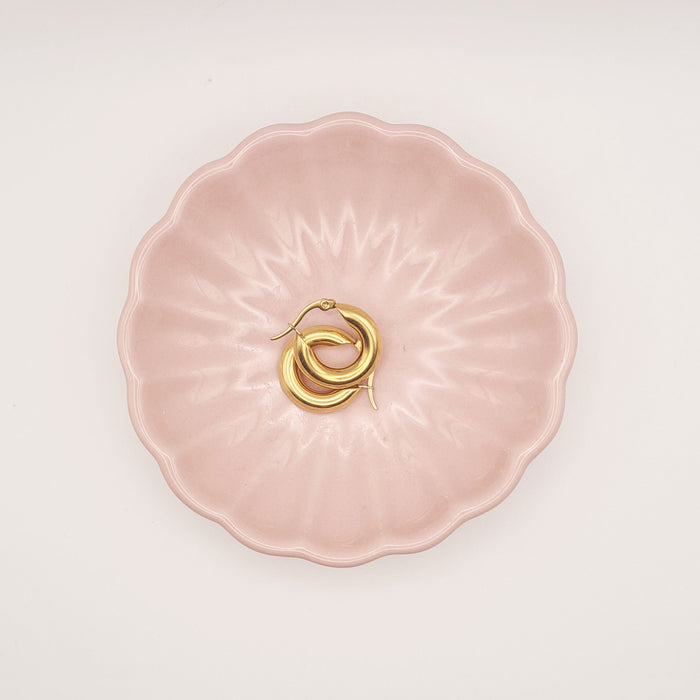 Small chubby hoop earrings in 18K gold-plated stainless steel by Forge and Lumber on a pink plate.