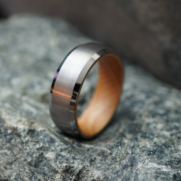 The Glencairn 8mm tungsten ring with barrel oak interior on a rocky background